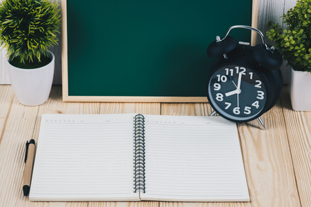 Blank green chalkborad and little tree with vintage alarm clock and notebook paper pen on wooden table with copy space for add text.の写真素材