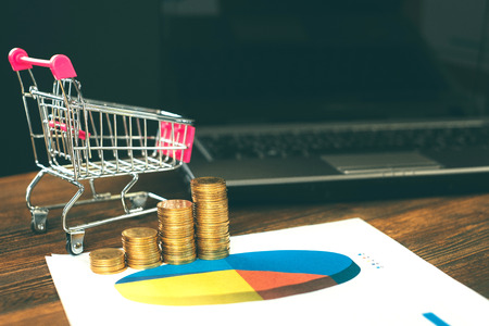 Step of coins stacks with trolley and notebook laptop computer and financial graph on paper on working table, business planning vision and finance analysis concept idea. and copy space for add text.の写真素材