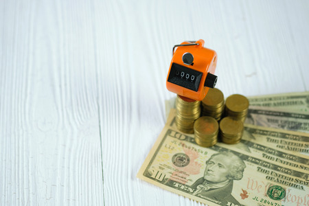 Tally counter or counting machine with 0000 number, coin and banknote on white wooden table,...