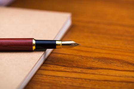 Fountain pen or ink pen with notebook paper on wooden working table with copy space, office desk concept idea.の写真素材