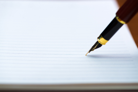 Close up of fountain pen or ink pen with notebook paper on wooden working table with copy space, office desk concept idea. shallow focus.の写真素材