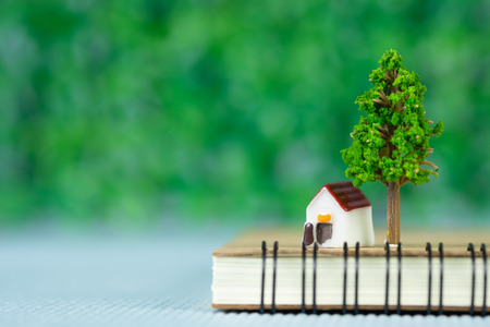 Small model house and little tree with notebook, savings banking, loan for house and real estate concept idea.の写真素材