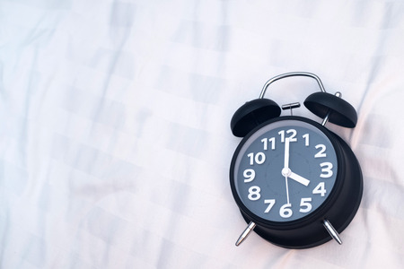 Vintage alarm clock on the bed in bedroom at home, wake up or bed time concept idea.の写真素材