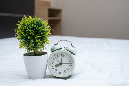 Vintage alarm clock and little decoration tree in white vase on the bed in bedroom at home, wake up or bed time concept idea.の写真素材