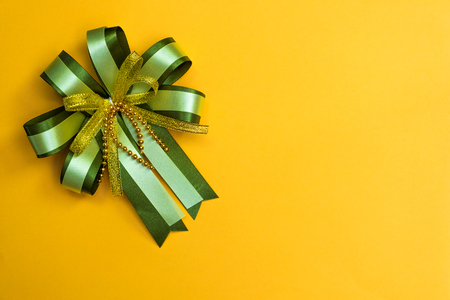 Decorative green ribbon bow on yellow background, view from above with copy space for add text, template for festival or promotion and special day concept idea.の写真素材