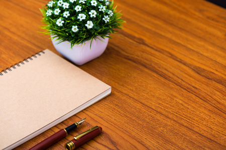 Fountain pen or ink pen with notebook paper and little decoration tree in white vase on wooden working table with copy space, office desk concept idea.の写真素材