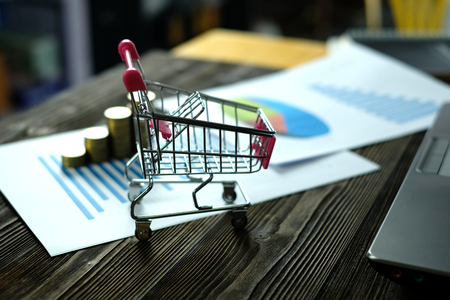 Step of coins stacks with trolley and notebook laptop computer and financial graph on paper on working table, business planning vision and finance analysis concept idea. and copy space for add text.の写真素材