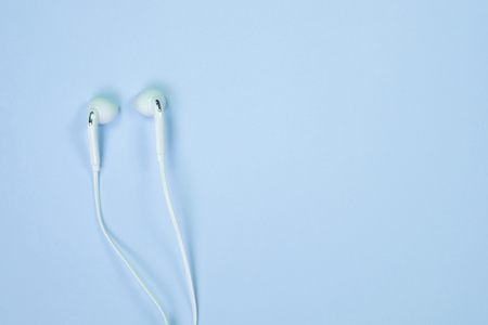 White Earphones or ear buds small talk on sweet blue colour pastel paper, top view, texture and...