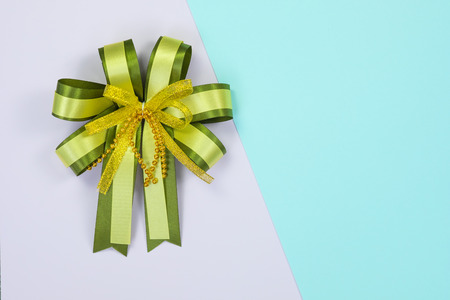 Decorative green ribbon bow on sweet pastel colored paper background texture, view from above with copy space for add text, template for festival or promotion and special day concept idea.の写真素材