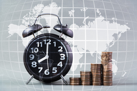 Alarm clock and step of coins stacks on working table, time for savings money, world map, global...