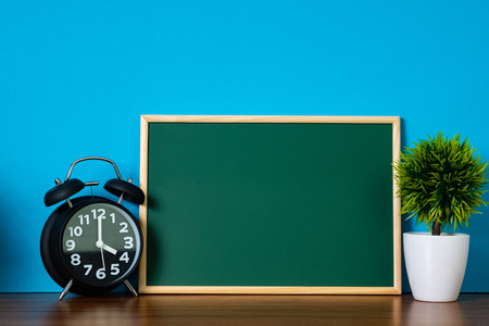 Blank green chalkborad with wood frame and little decorative tree in white vase and vintage alarm...