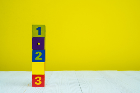 Square block puzzle number 1 2 and 3 on table with yellow wall background