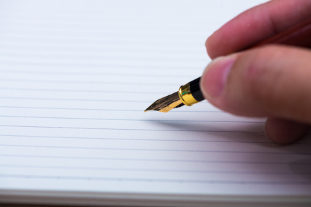 Man hand writing with fountain pen or ink pen with notebook paper on wooden working table with copy space, office desk concept idea.の写真素材