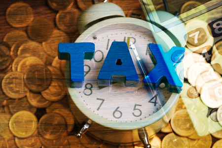 Double exposure Time to pay TAX concept. TAX alphabet with stack of coin and vintage alarm clock with office supplies or office work essential tools or itemsの写真素材