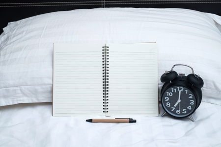 Diary or notebook and vintage alarm clock on bed in bedroom at home or hotel, working or note something before sleep.の写真素材