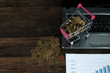 Step of coins stacks with trolley and notebook laptop computer and financial graph on paper on...