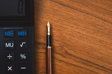 Fountain pen or ink pen with calculator on wooden working table with copy space, office desk concept idea.の写真素材