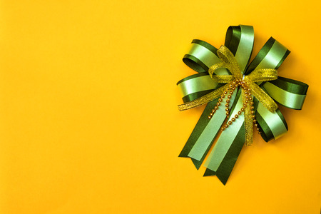 Decorative green ribbon bow on yellow background, view from above with copy space for add text, template for festival or promotion and special day concept idea.の写真素材