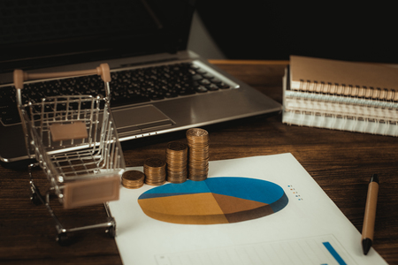 Step of coins stacks with trolley and notebook laptop computer and financial graph on paper on working table, business planning vision and finance analysis concept idea. and copy space for add text.の写真素材