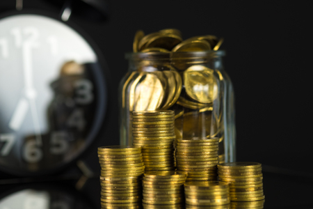 Coins stacks with coin in glass jar bottle and alarm clock in dark room, business and finance concept idea.の写真素材