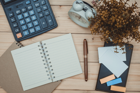 Office supplies or office work essential tools items on wooden desk in workplace, pen with notebook and calculator and alarm clock with copy space, top viewの写真素材