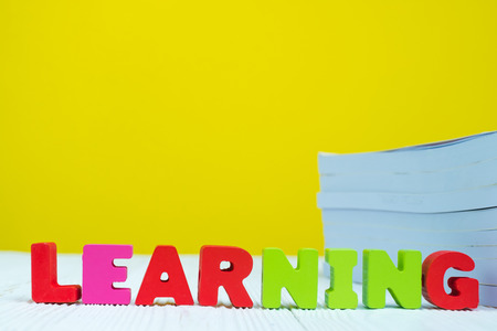 LEARNING text alphabet and pile of book on white table with yellow wall background.