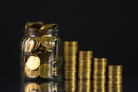 Coins stacks and gold coin money in the glass jar on dark background, for saving for the future banking finance concept idea.の写真素材