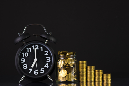 Coins stacks with coin in glass jar bottle and alarm clock in dark room, business and finance concept idea.の写真素材