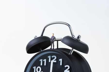 Figure miniature businessman or small people standing with alarm clock, time for savings money concept or business financial idea.の写真素材