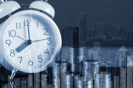 Double exposure of coin stack and alarm clock with city background and financial graph, business finance concept idea.の写真素材