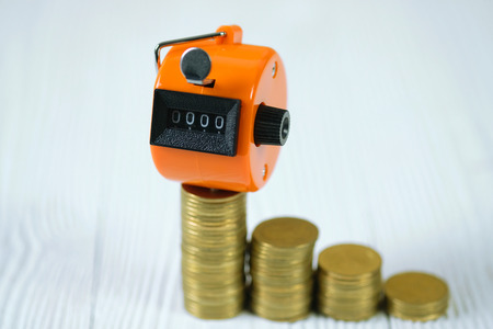 Tally counter or counting machine with 0000 number, step of coin stack on white wooden table,...