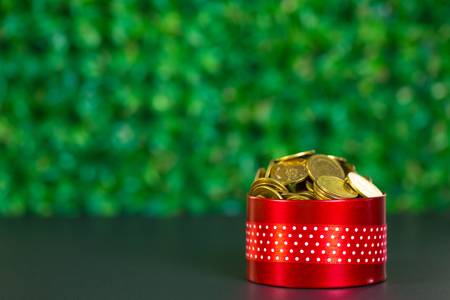 Round red gift box with ribbon bow on black table and green background with copy space for season or greeting and merry concept, present on holiday.の写真素材
