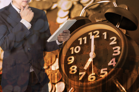 Double exposure of alarm clock and coins stacks with city background businessman and finance graph, time for savings money concept, banking and business concept idea.の写真素材