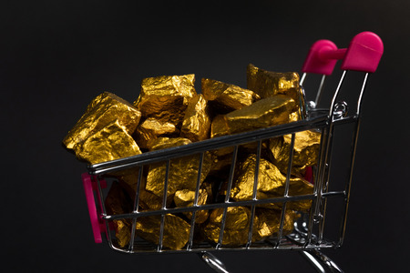 A pile of gold nuggets or gold ore in shopping cart or supermarket trolley on black background,...