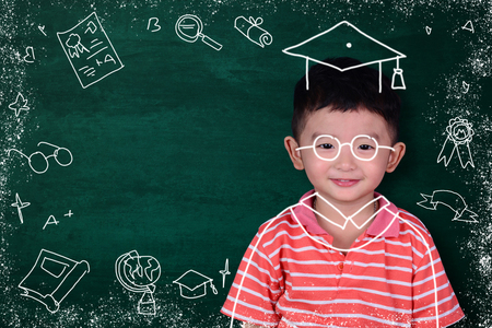 Asian kid imagine his graduated day with hand drawn graduate dress and stationery supplies school object activities for learning on green chalkboard background, education and graduation concept idea.の写真素材