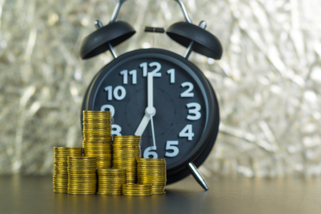 Alarm clock and coins stacks on working table, time for savings money concept, banking and business concept idea.の写真素材