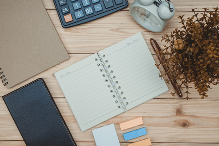 Office supplies or office work essential tools items on wooden desk in workplace, pen with notebook and calculator and alarm clock with copy space, top viewの写真素材
