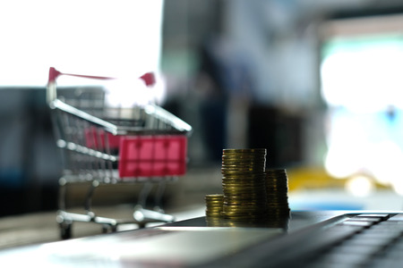 Step of coins stacks with trolley and notebook laptop computer and financial graph on paper on working table, business planning vision and finance analysis concept idea. and copy space for add text.の写真素材