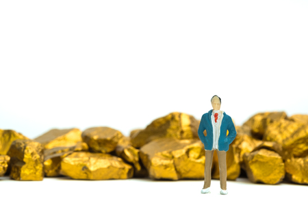 Figure miniature businessman or small people with pile of gold nuggets or gold ore on white background, precious stone or lump of golden stone, financial and business concept idea.の写真素材