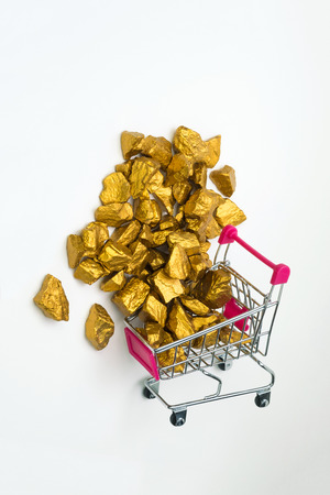 Pile of gold nuggets or gold ore in shopping cart or supermarket trolley on white  background, precious stone or lump of golden stone, financial and business concept idea.の写真素材