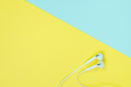 White Earphones or ear buds small talk on sweet blue and yellow colour pastel paper, top view, texture and background. music listening concept idea.の写真素材