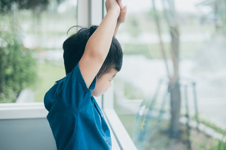 Alone Asian boy looking out of the window, waiting for someone.の写真素材