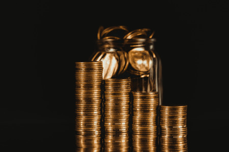 Coins stacks and gold coin money in the glass jar on dark background, for saving for the future banking finance concept idea.の写真素材