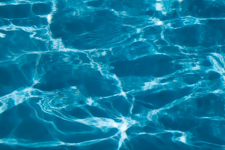 Blue and bright ripple clean water surface in swimming pool with sun reflection.