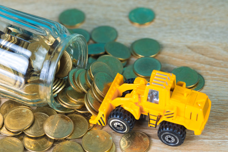 Mini bulldozer truck loading stack coin with pile of gold coin to glass jar, business finance and banking industrial concept idea.の写真素材