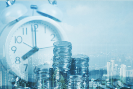 Double exposure of coin stack and alarm clock with city background and financial graph, business finance concept idea.の写真素材