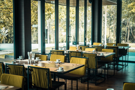 Empty restaurant part of hotel resort with table and armchair near windows and garden view.