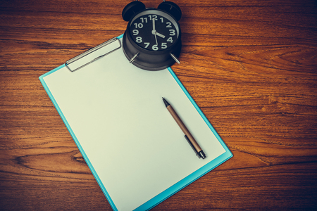 Black vintage alarm clock with clipboard and blank white paper and pen, copy space for add your text, work on time or over time and deadline concept idea.の写真素材
