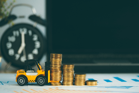 Miniature mini forklift truck with coin stack on working table with office supplies or office work essential tools items for business financial conceptの写真素材