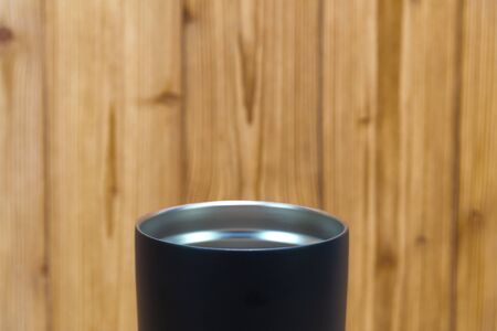 Black colour stainless steel tumbler or cold and hot storage cup on wooden background.